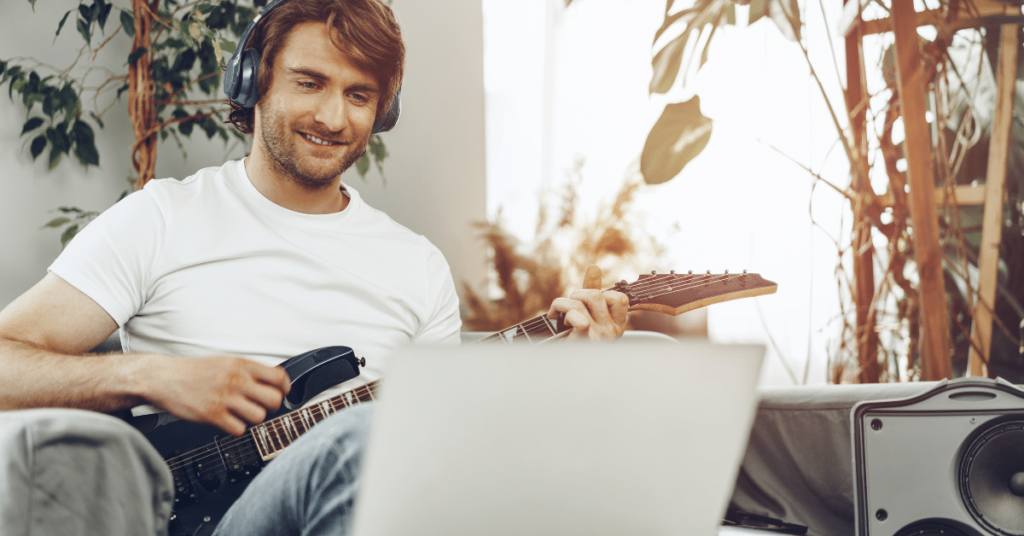 Student lernt E-Gitarre online auf der Couch mit Laptop – fortgeschrittener Rock & Pop E-Gitarrenkurs mit Abschluss der New Music Academy.